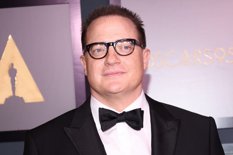 Closeup of Brendan Fraser wearing a suit and thick black glasses against a purple backdrop featuring the Academy of Motion Picture Arts and Sciences' logo and the words Oscars 95.