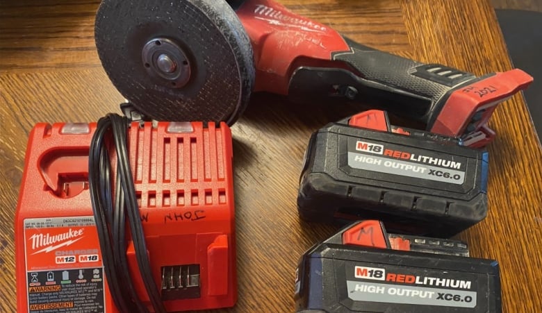 A grinder, two batteries and a charger lay on a wood table. 