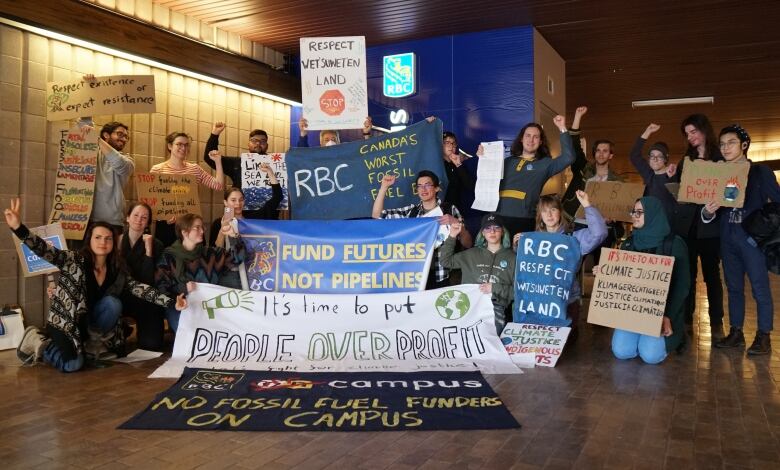 A group of students holding protest signs pose for a group photo. Many of them have their arms raised.