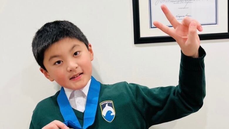 Young boy with peace sign and holds a medal in his other hand. 