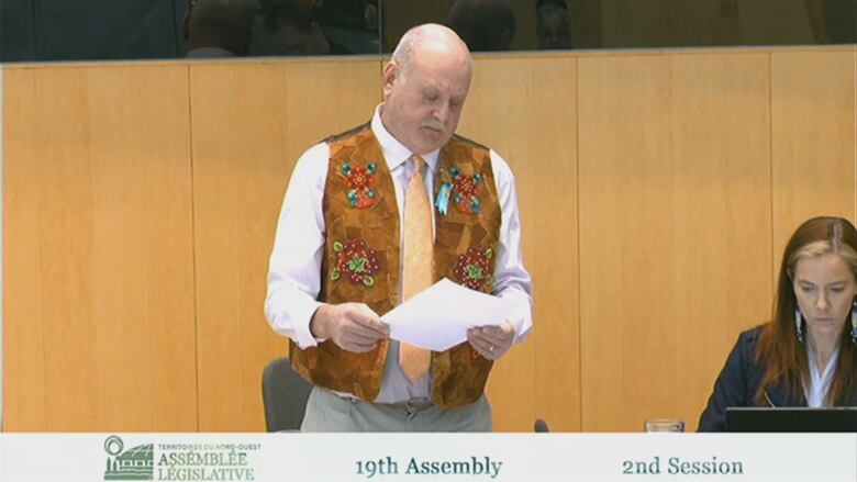 Man in suede vest, standing at desk. 