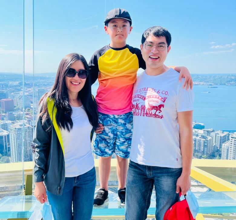 A family of three are standing in front of a view of downtown Seattle