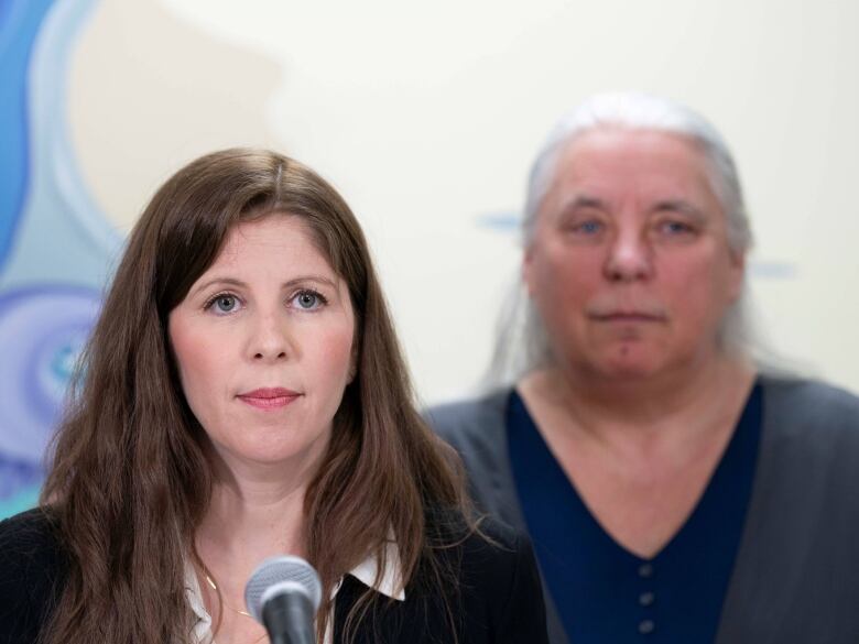 Two women stand before a microphone. 