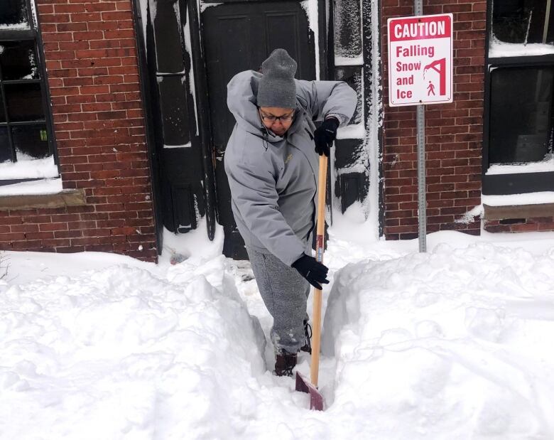 A woman in winter gear shovels snow.