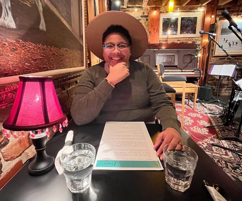 A woman in a wide brimmed hat sits at a restaurant table.