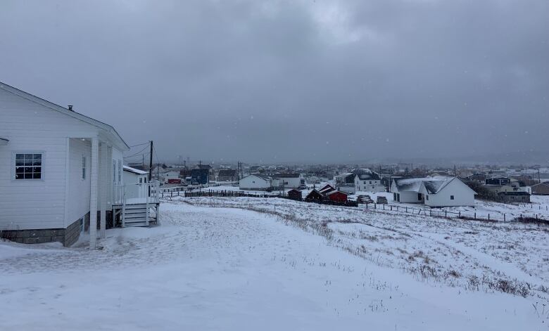 A snowy field with fences crossing it. Houses are in the distance on the left and water is in the distance on the right.