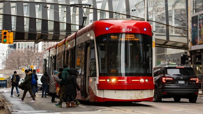 People board a streetcar at a busy downtown intersection.