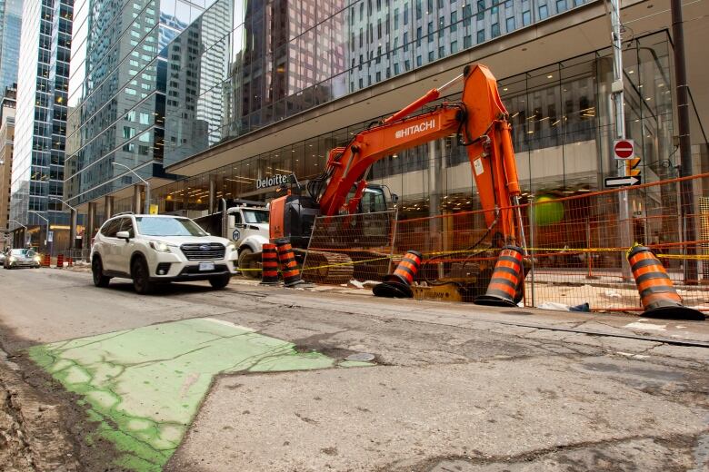 A car drives by a large construction site on a city street.