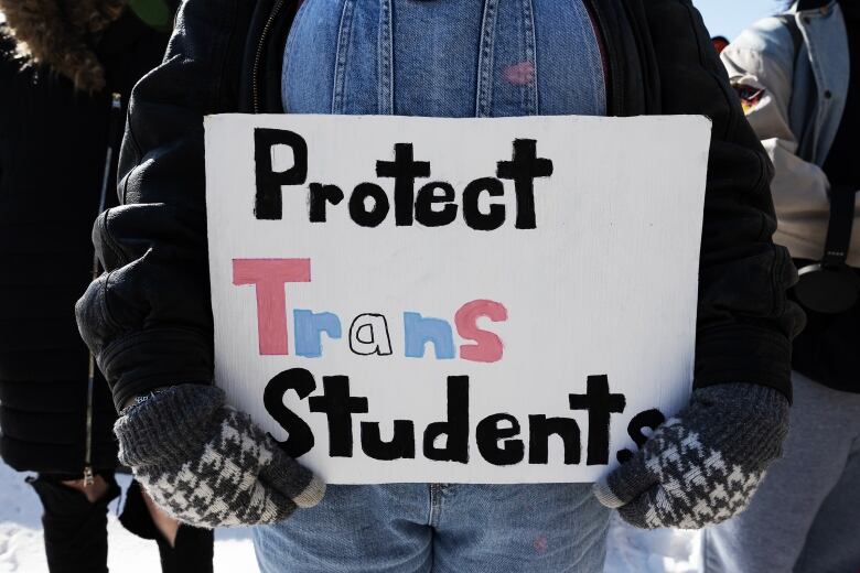 A person holds up a sign that reads 'protect trans students.'