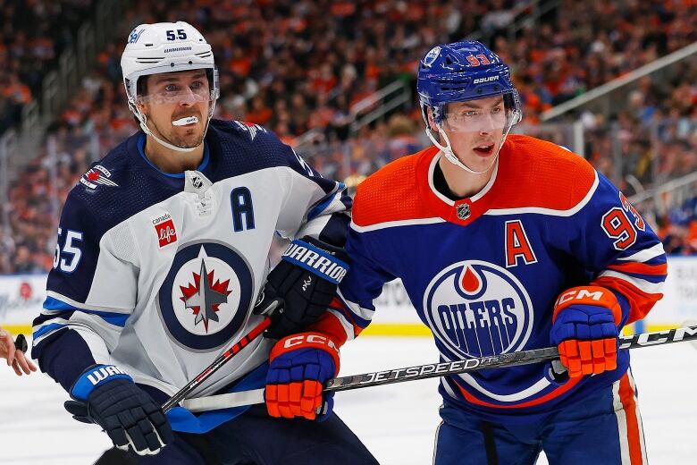 Two male ice hockey players touch elbows while battling for position on the ice.