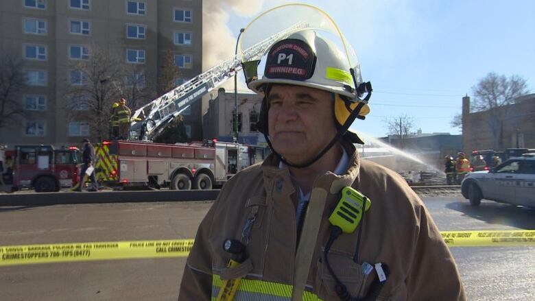 A man in fire gear stands across the street from a fire.