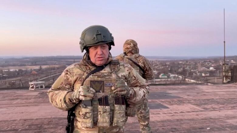 A man in a helmet and battle fatigues is shown speaking while looking at a camera.