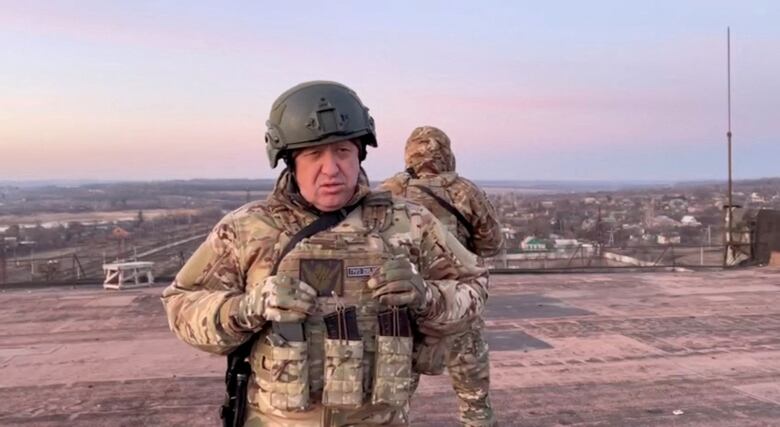 A man in a helmet and battle fatigues is shown speaking while looking at a camera.