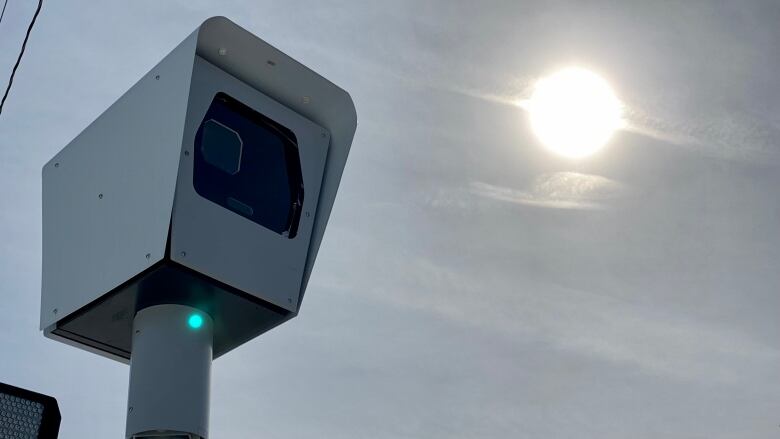 A camera on a post in front of the sky and sun.