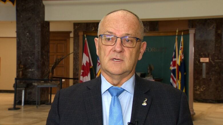 A man wears glasses and a black suit jacket with a blue tie.