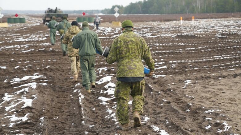 Soldiers walk toward a tank in a field in Poland