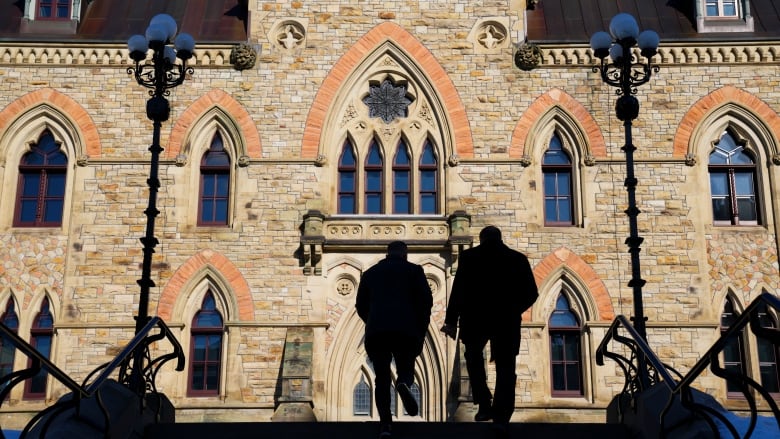 Two people silhouetted by the sun as they climb stairs toward a large stone building.