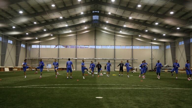 A line of soccer players dressed in blue stretch inside an indoor soccer facility. 