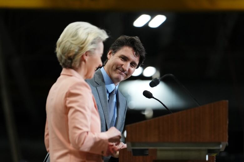 Prime Minister Justin Trudeau looks on as European Commission President Ursula von der Leyen speaks at a podium. 