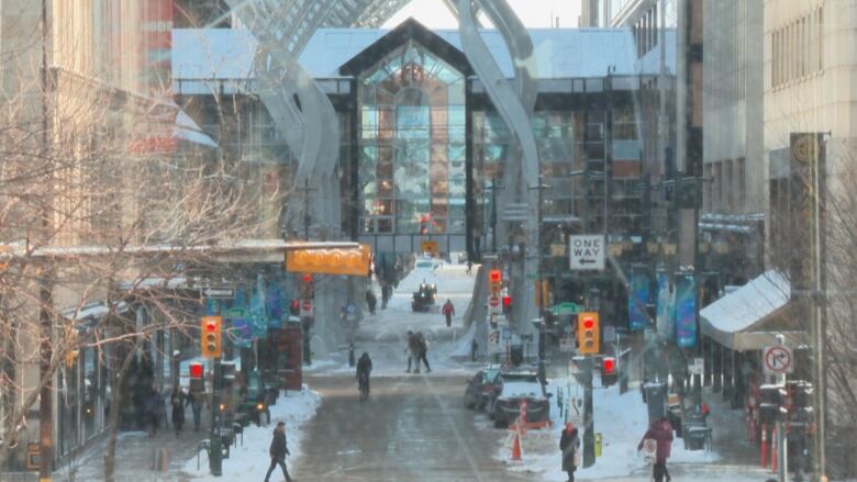 The image shows several pedestrians walking around a busy intersection with snow on the ground. 