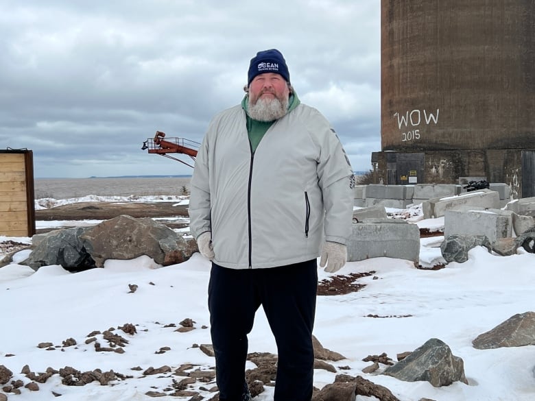 A man wearing winter clothes stands outside on a snowy seashore.