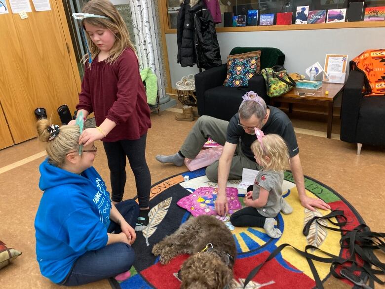 Two adults play with two young girls on a rug at Wahkohtowin. 