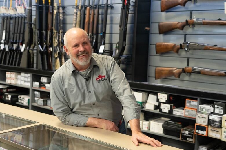 A man poses in front of a wall of guns.