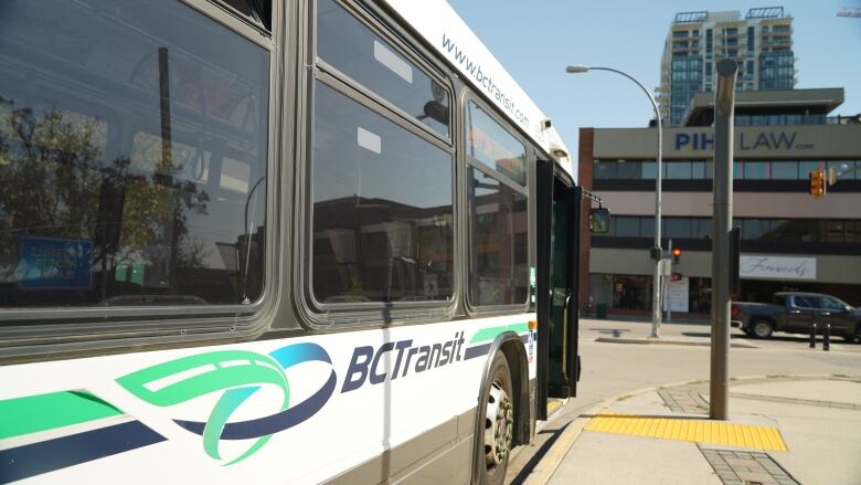 A B.C. Transit bus sits at a bus stop with a building in the background.