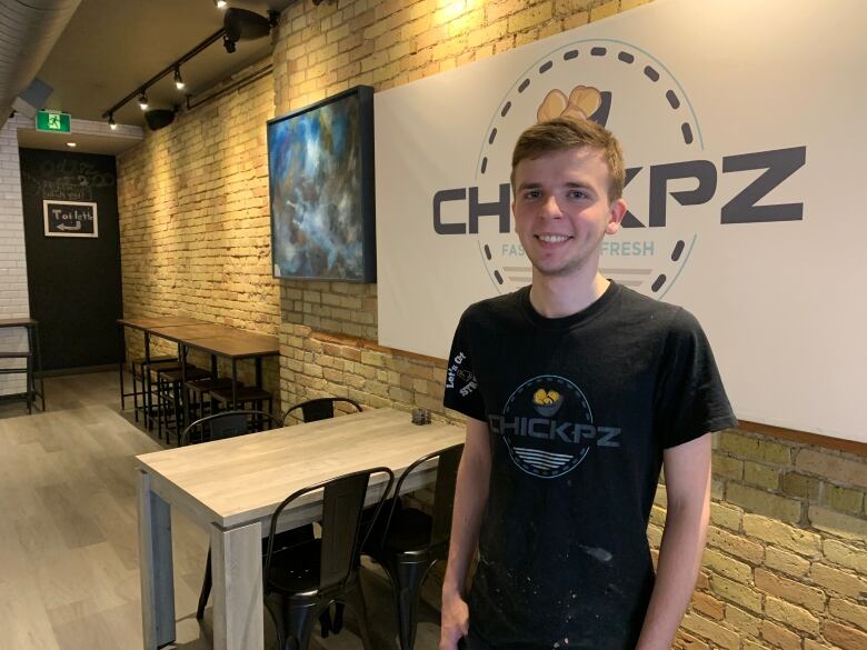 Nykyta Rylstov, a line cook, standing in front of a ChickPZ sign in a black shirt.