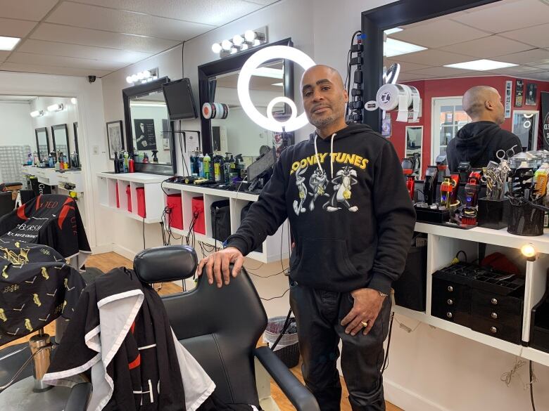 Man standing beside a barber chair in front of barber tools.