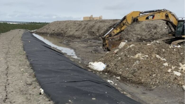 A crack in the dirt, plastic sheeting, a digger and two holding tanks on the horizon. 