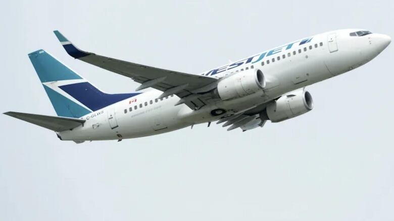 A white passenger airplane rising in the sky with the green and teal WestJet markings on it's tail and fuselage.