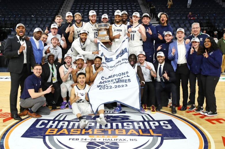 A basketball team and its staff pose with their championship banner.