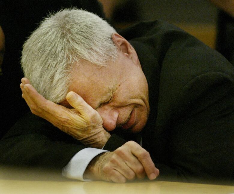 A man holds his hand to his head while leaning over a table.