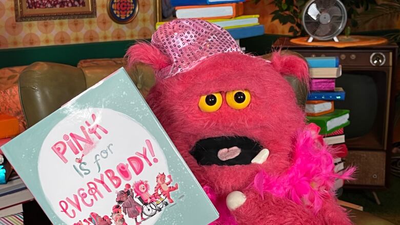 A pink puppet holding up a children's picture book.