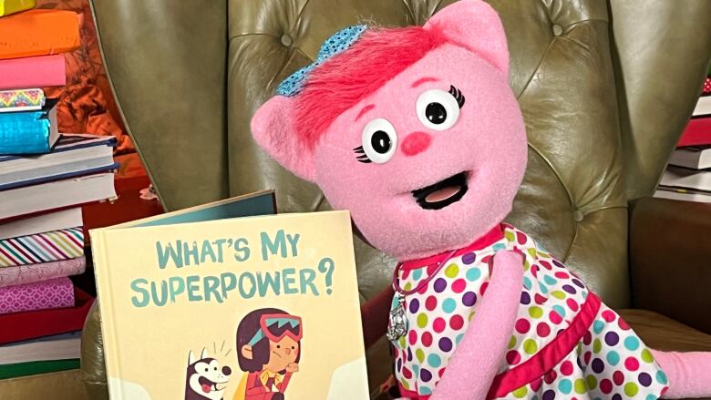 A pink cat puppet holds up a children's picture book, smiling.