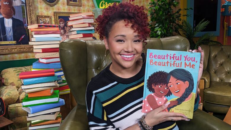 A woman holds up a children's picture book, smiling.