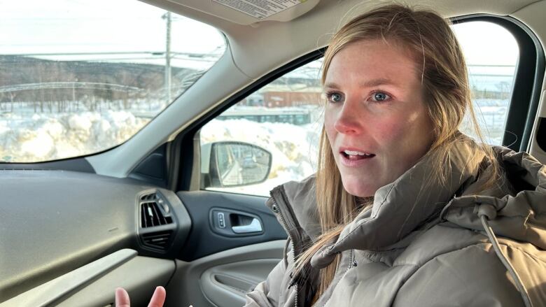 A woman in a parka talks while sitting in the passenger seat of a vehicle. 