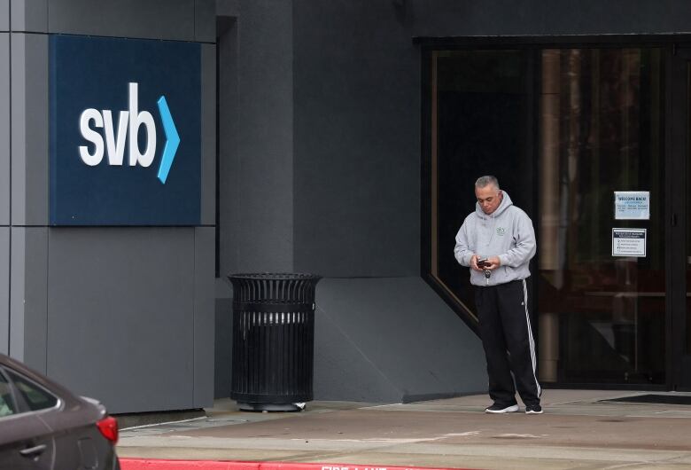 A man checks his phone while standing outside an office building. 