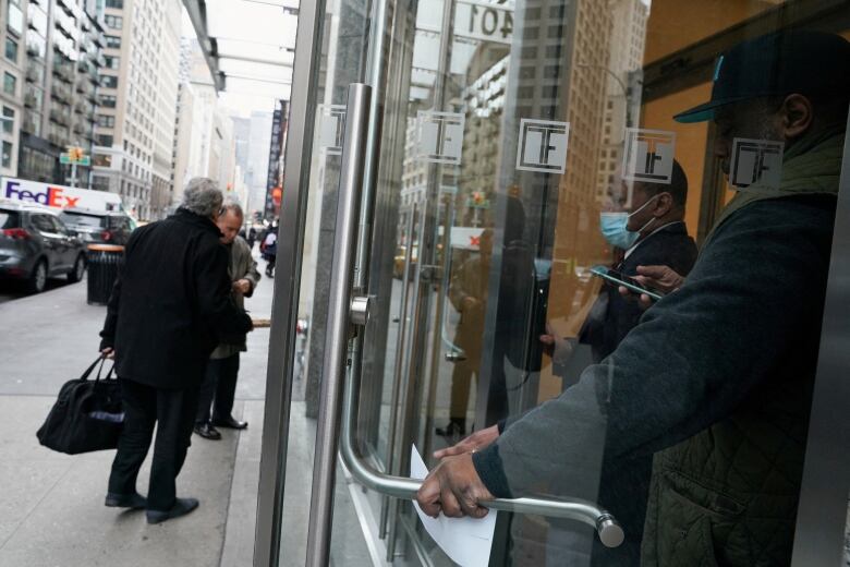 Two men stand outside the closed doors of a bank. Two other men stand inside. 