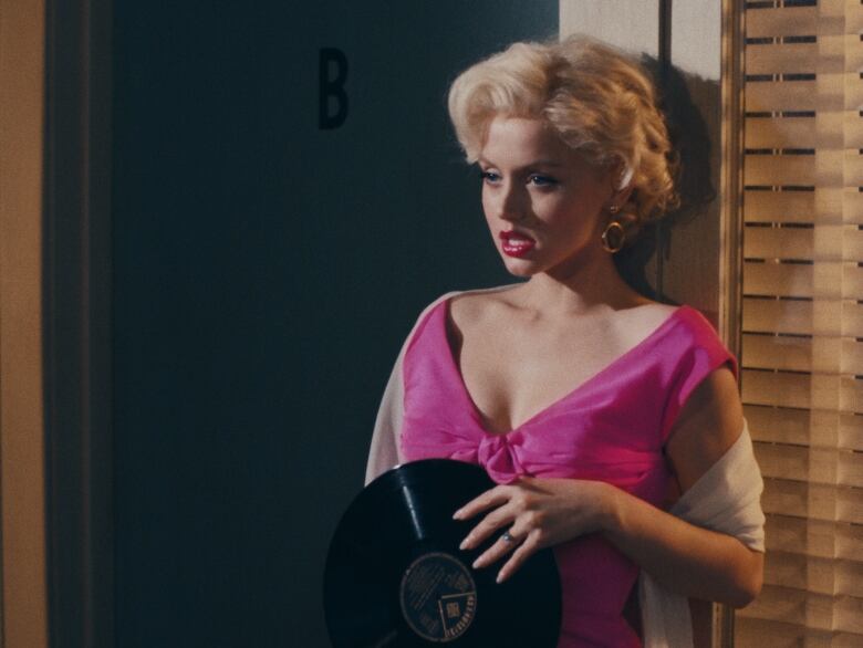 A woman in a pink dress holds a vinyl record.