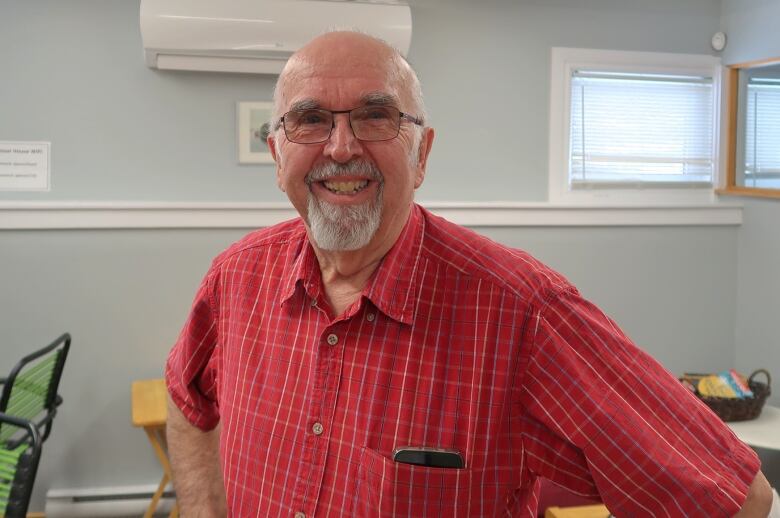 A smiling man with glasses in a red patterned shirt smiles at the camera.