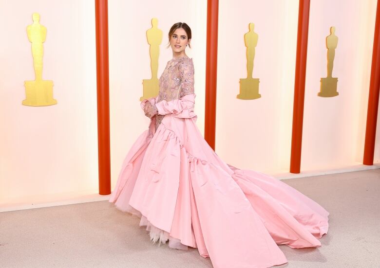 A woman wears a pale pink gown with a sequined body and long skirt.