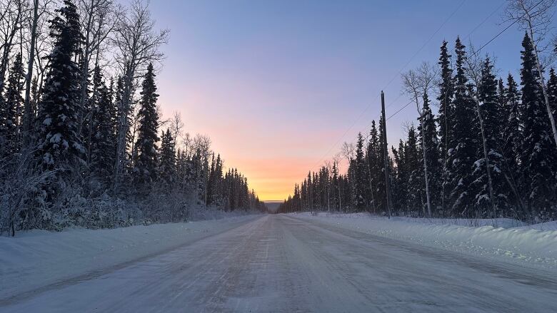 The photo shows an icy road with a pink sky. 