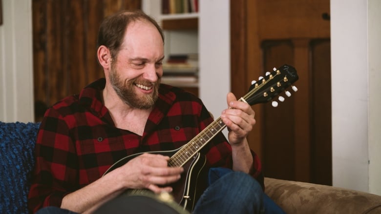 A smiling, balding man holds a mandolin.