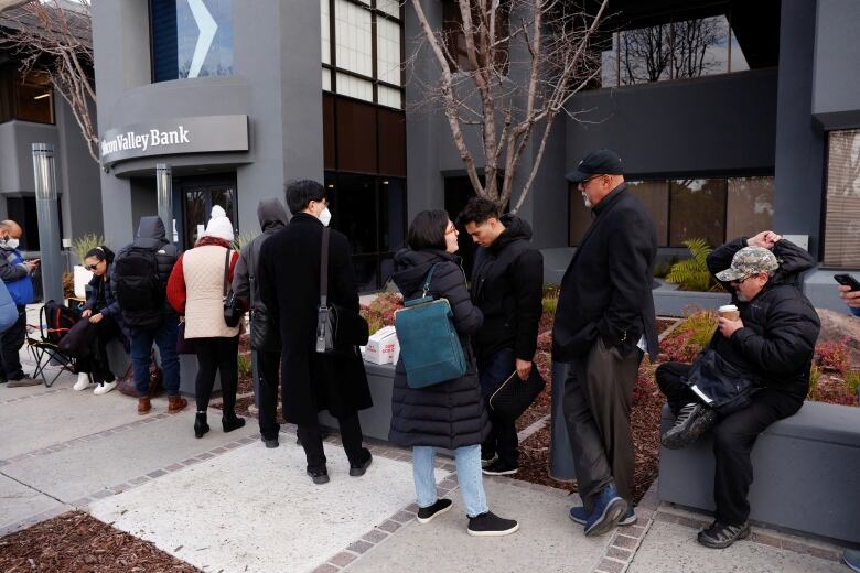 People lined up on a sidewalk outside a building with a sign reading Silicon Valley Bank.