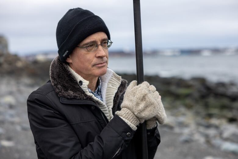 A man wearing a toque and gloves stands at the edge of the water.