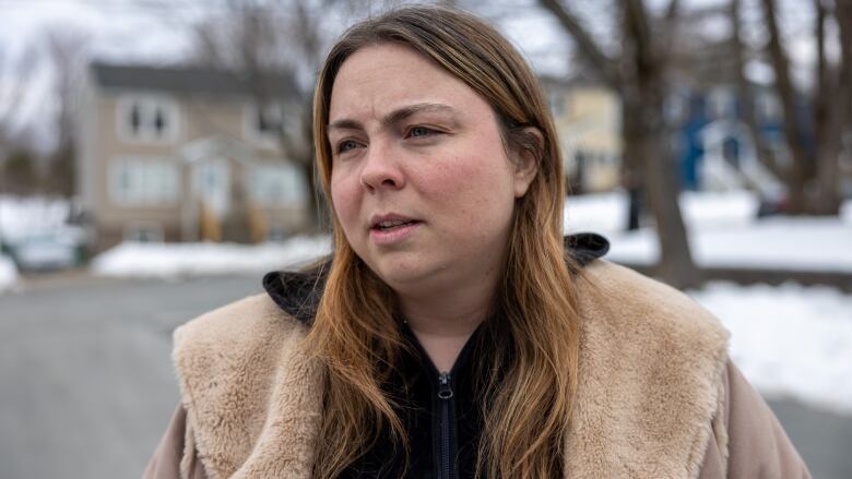 A woman stands in front of the house and looks at the camera. 