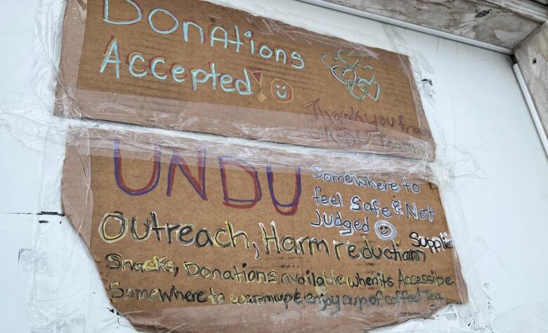 A wooden sign on the door of a trailer says Donations Accepted and UNDU  Outreach, Harm reduction.