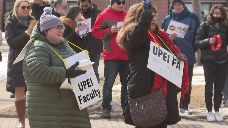 Faculty members at UPEI hold signage and cheer in the campus quad.  